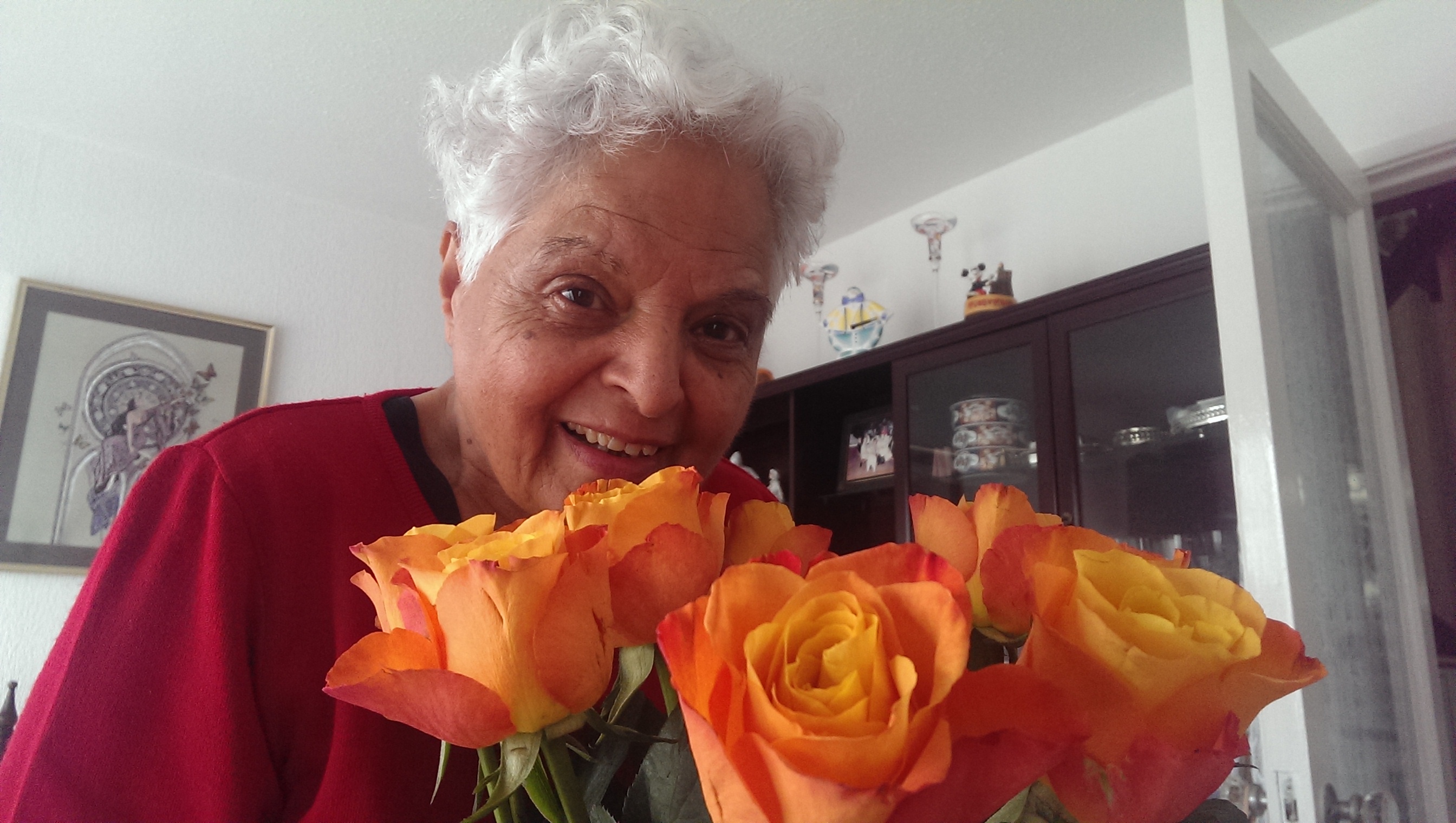 Surjit smiling warmly behind a bouquet of orange roses