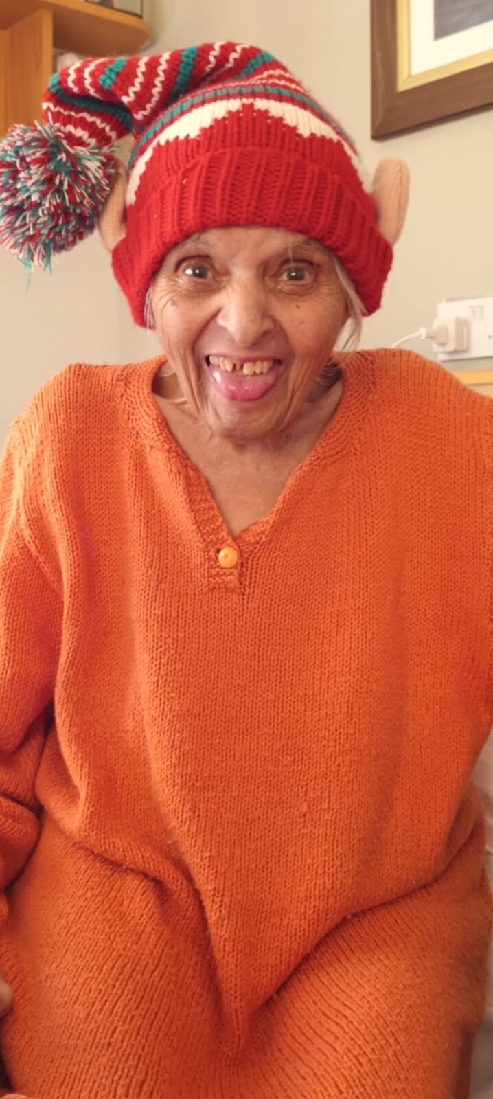 Surjit laughing joyfully in a colourful festive knitted hat and orange jumper