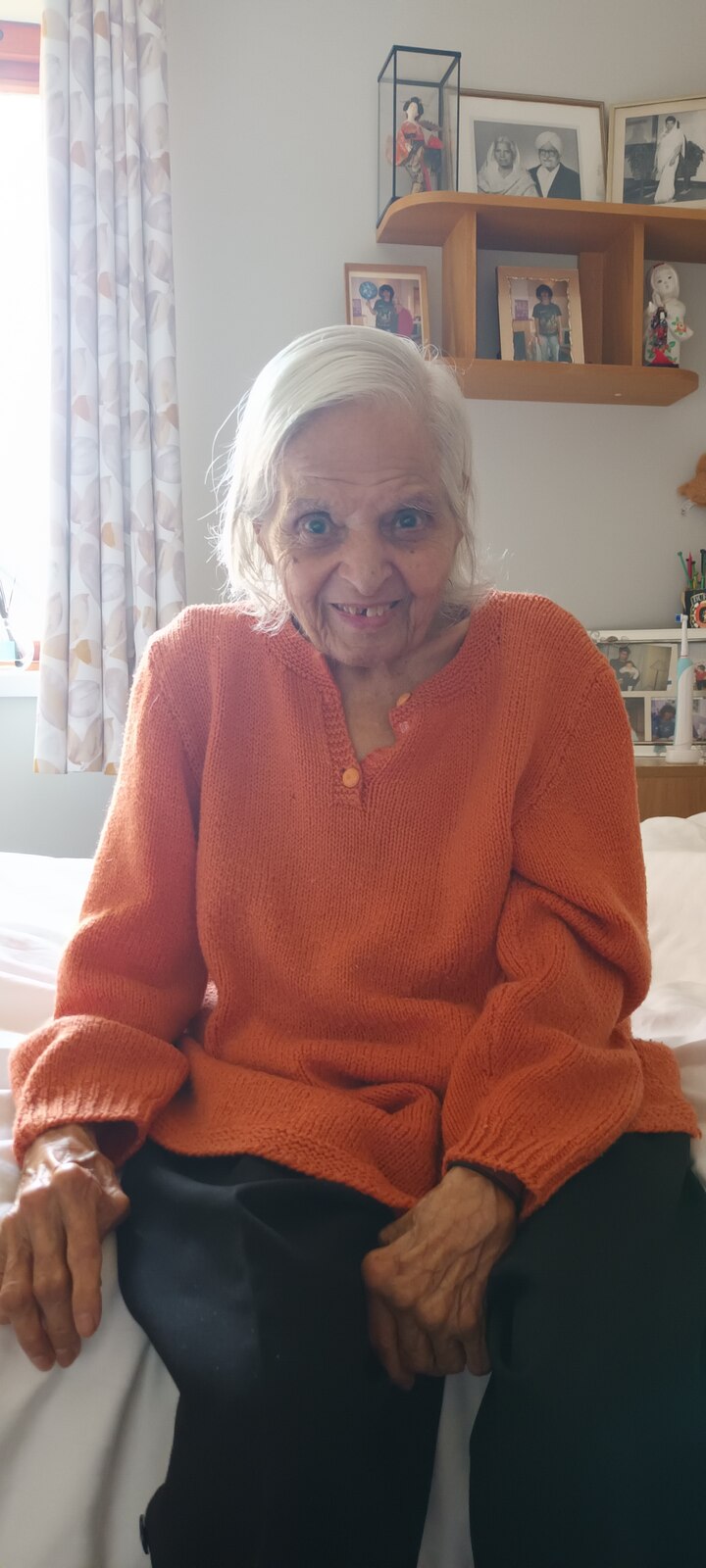 Surjit beaming in her favourite orange cardigan, framed photos behind her