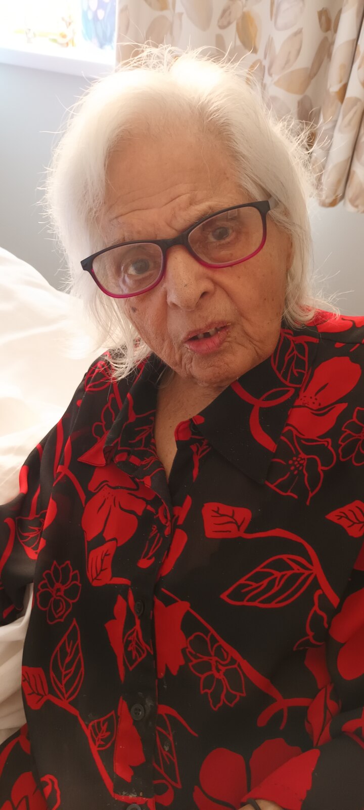 Surjit in a striking red and black floral top with her glasses on