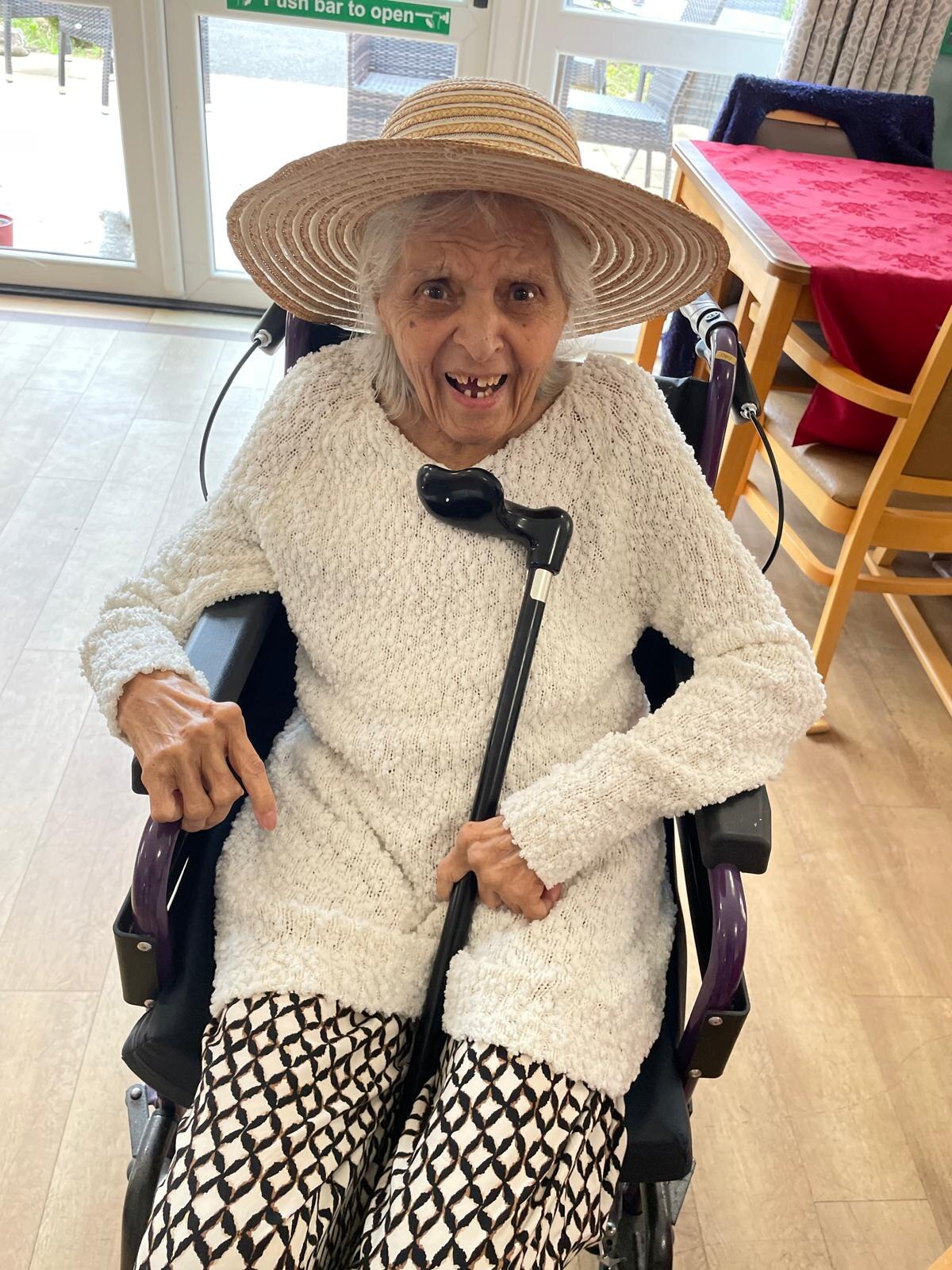 Surjit with a big joyful smile wearing a straw sun hat and white cardigan